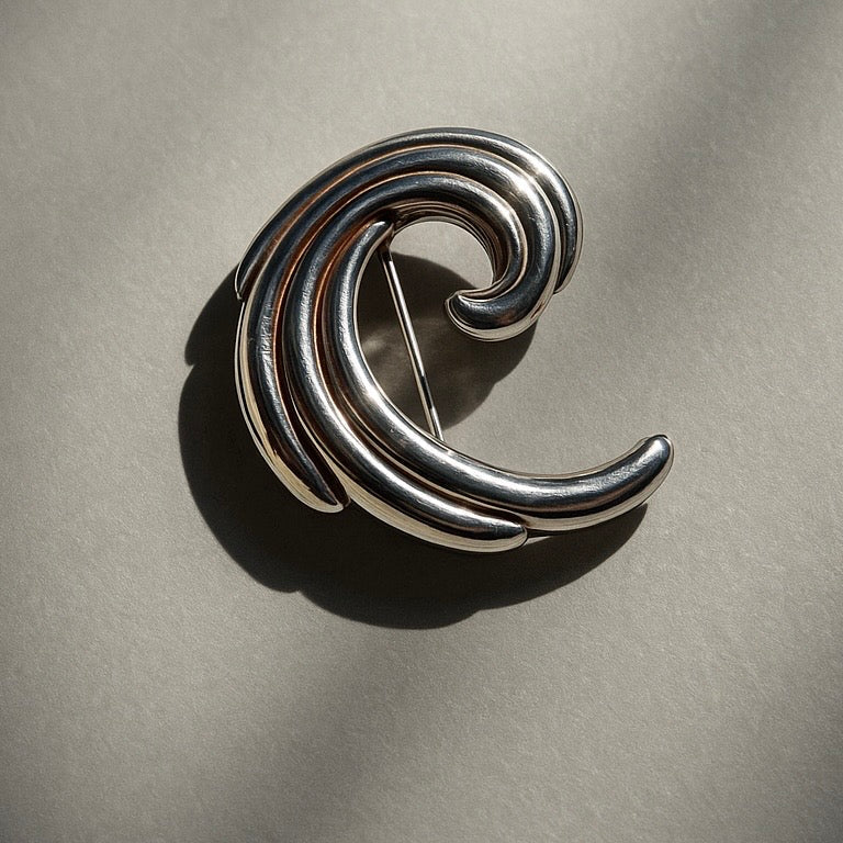 Silver brooch with a wave design on a gray background