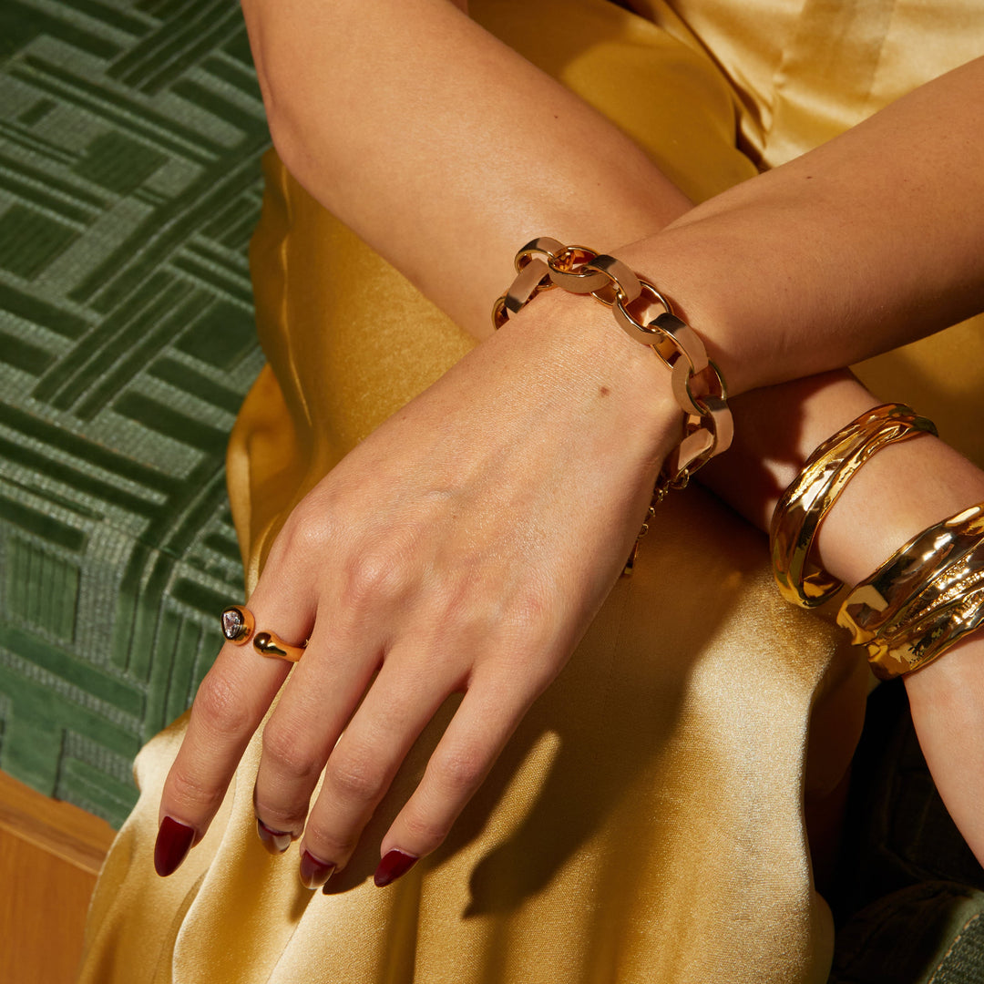 Person wearing gold bracelets and rings on a patterned green and brown background