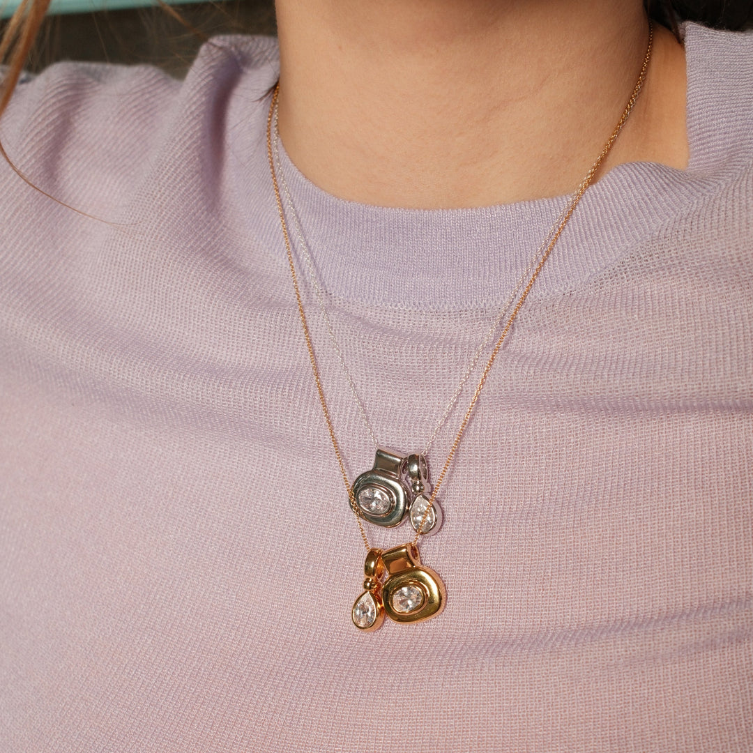 Necklace with two pendants worn by a person in a light purple shirt.